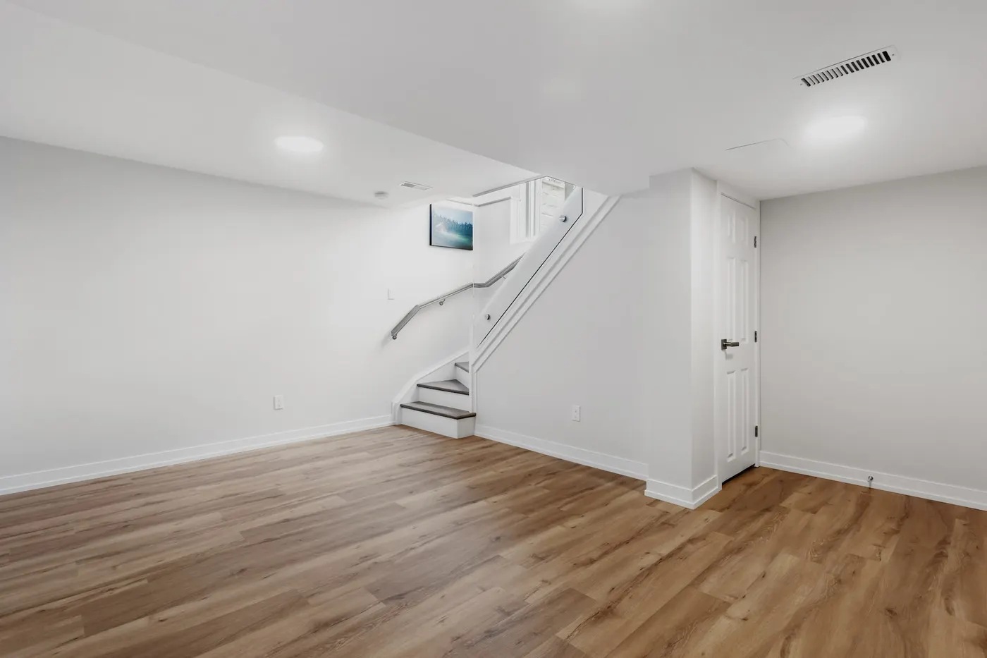 A finished basement with plank flooring, recessed lights and stairs