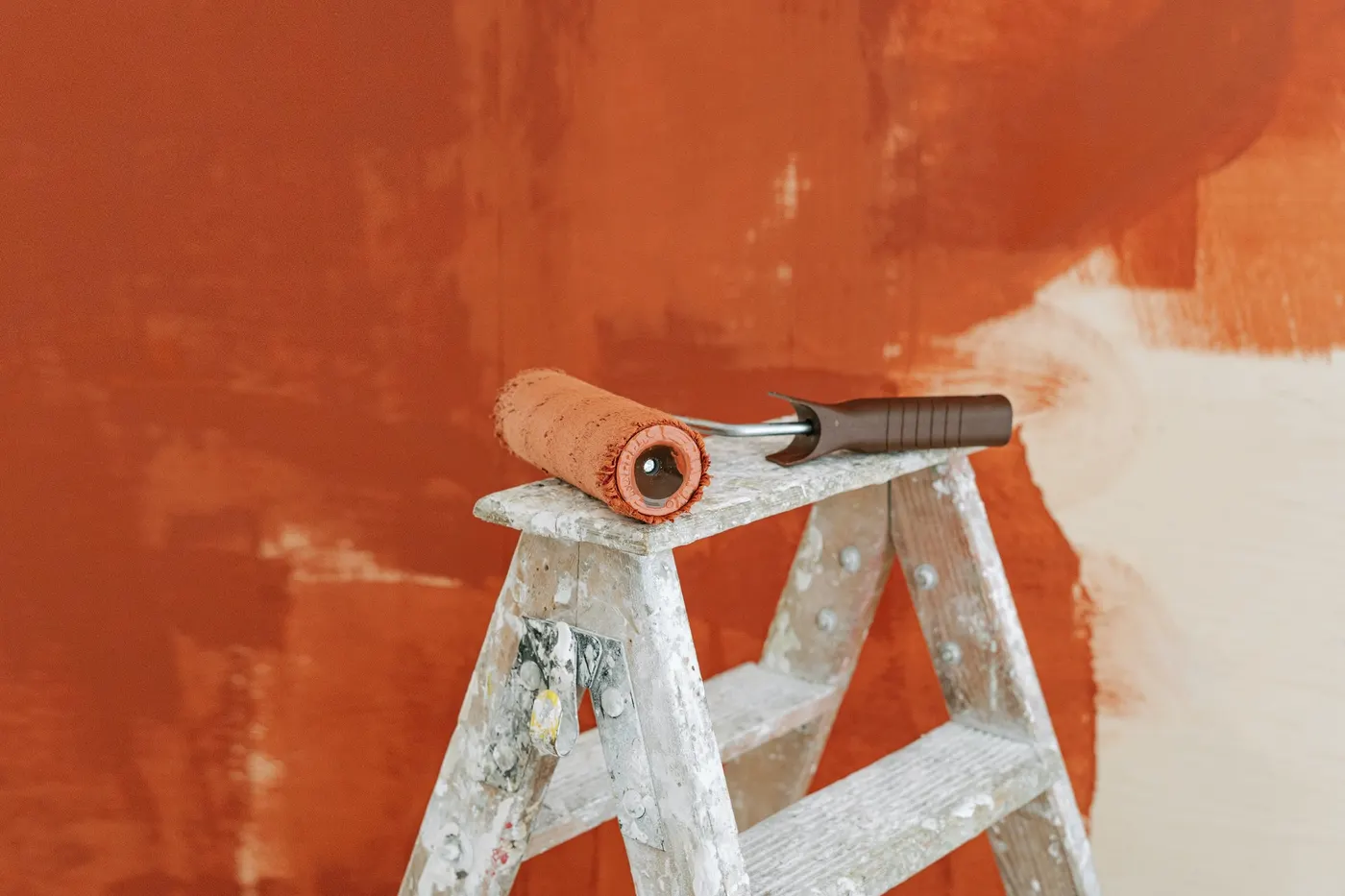 A paint roller on a stepladder against a half-painted wall
