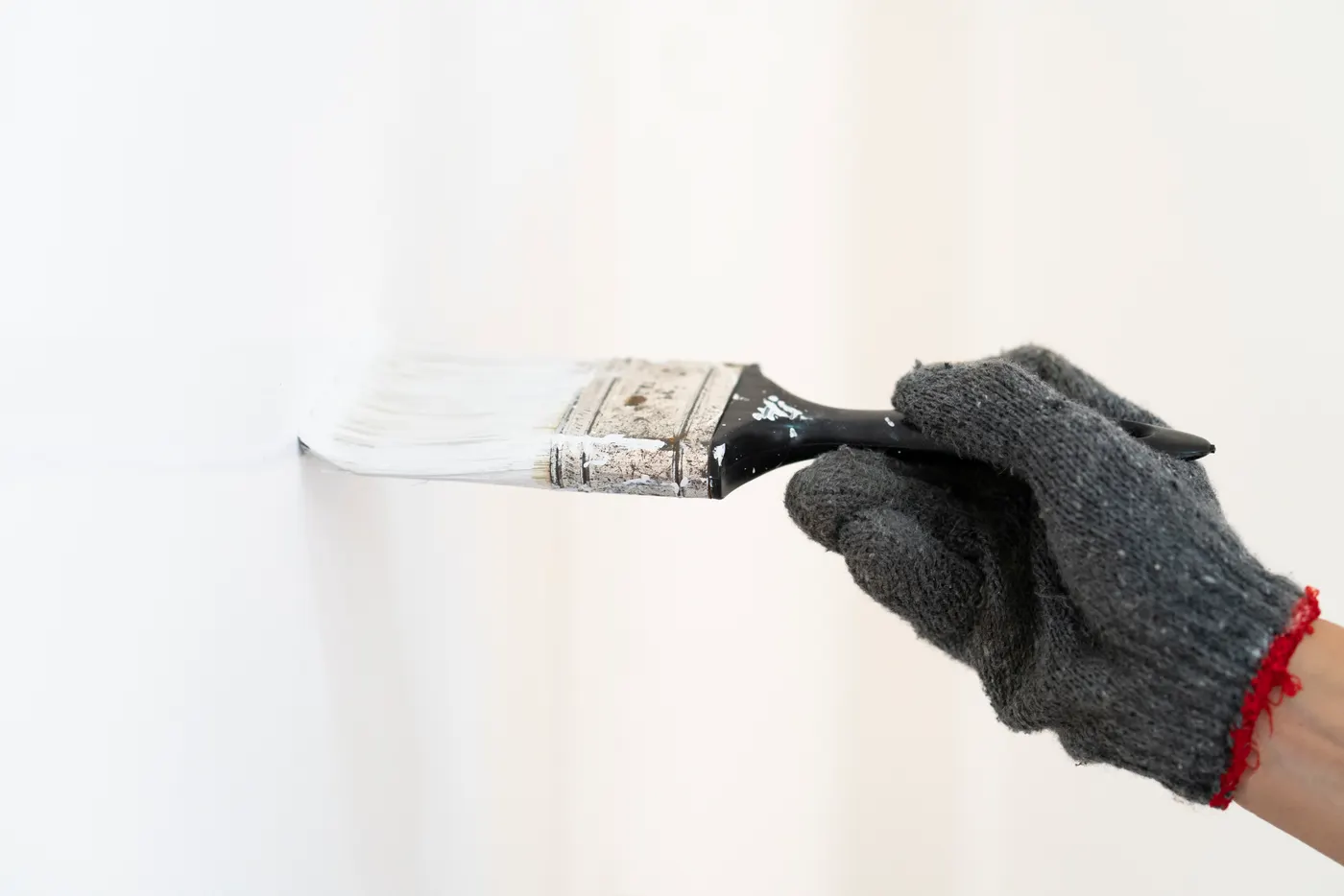 A gloved hand brushing white paint onto a wall