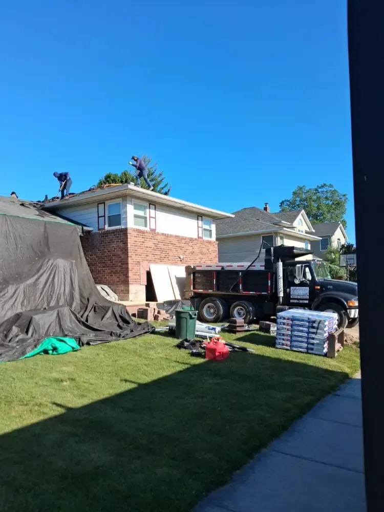 Tarps over the siding and a dump truck on site during a roof replacement